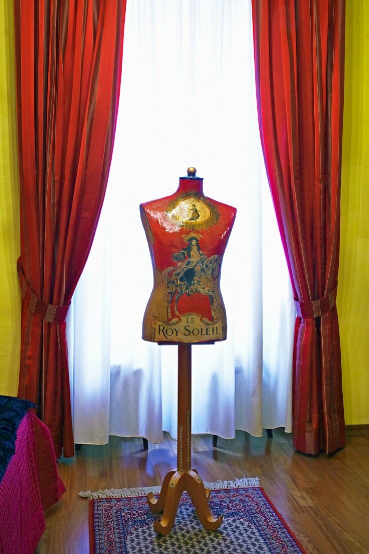 Vintage Schneiderpuppe vor Fenster mit gerafftem rotem Vorhang und transparenter Gardine