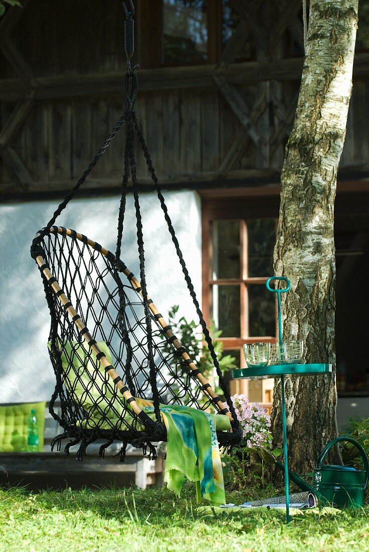 Hängestuhl aus Netzstoff an Baum vor rustikalem Bauernhaus