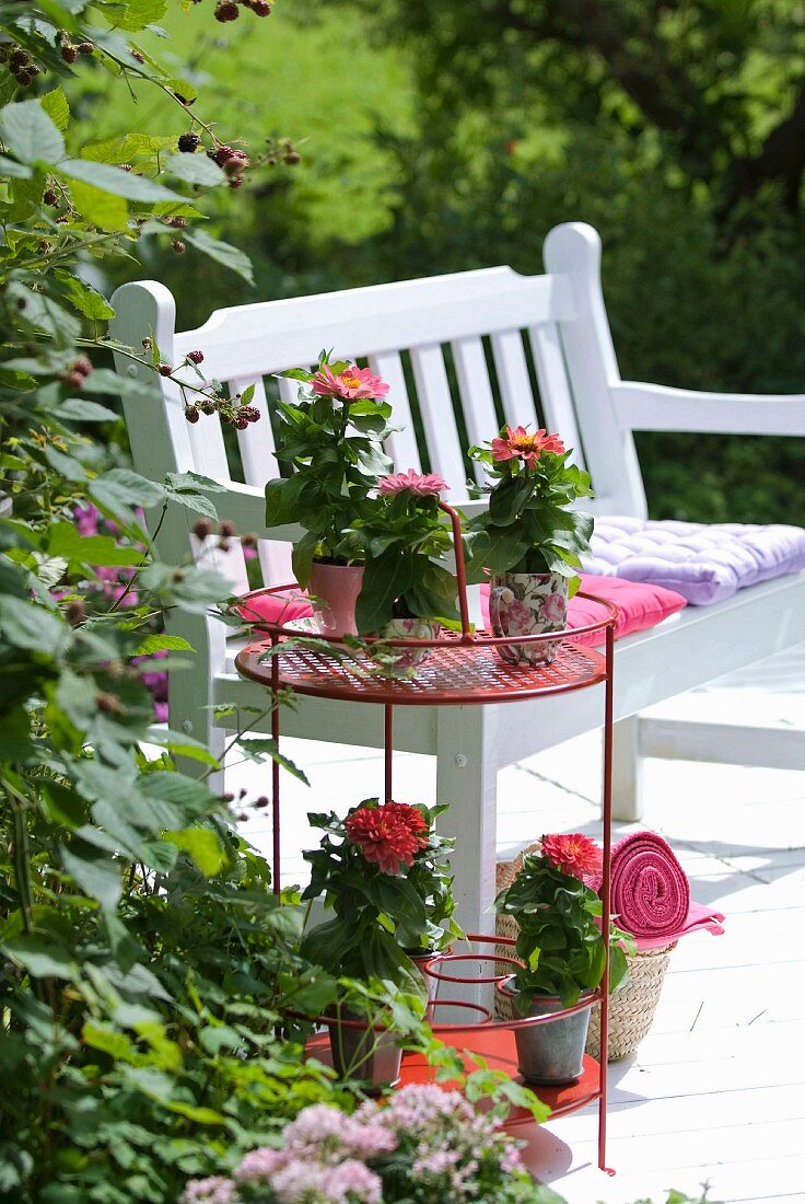 Terrassenplatz im romantischen Landhausstil mit Deko in Pinktönen zu weisser Holzbank und rotem Beistelltisch mit Blumentöpfen