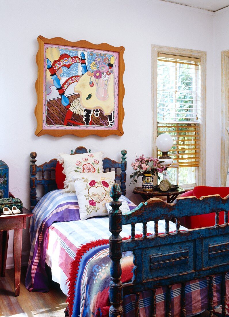 Antikes, blaues Landhausbett mit bunter Bettwäsche unter modernem Pop Art Gemälde