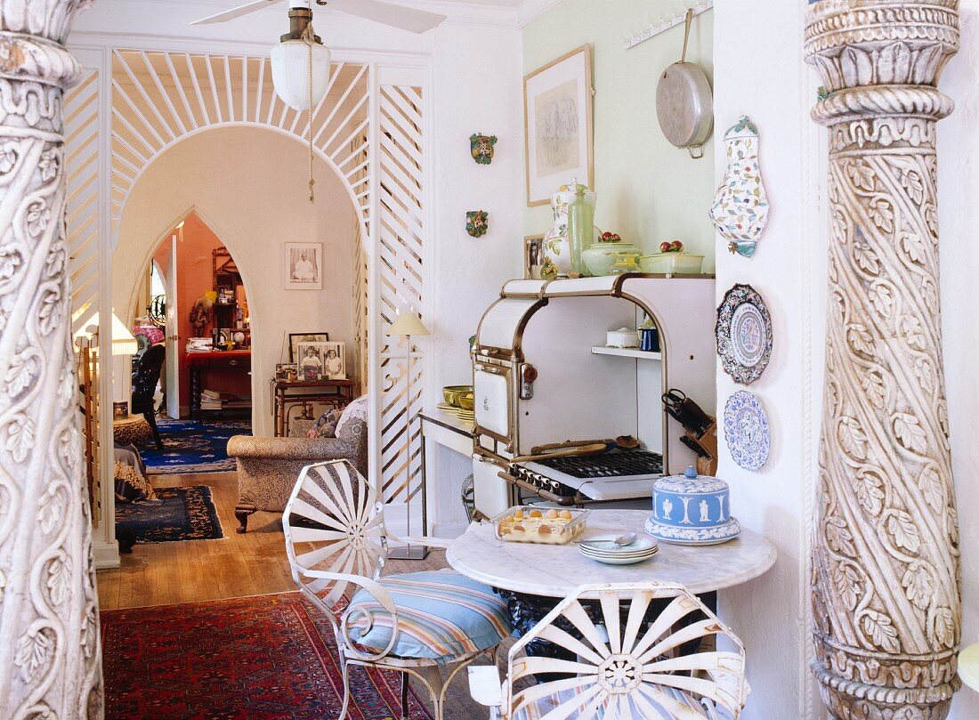 Ornamentierte Säulen und ein halbtransparenter Rundbogendurchgang trennen die Küche mit Vintage-Holzherd und ausgefallenen Eisenstühlen vom Wohnbereich