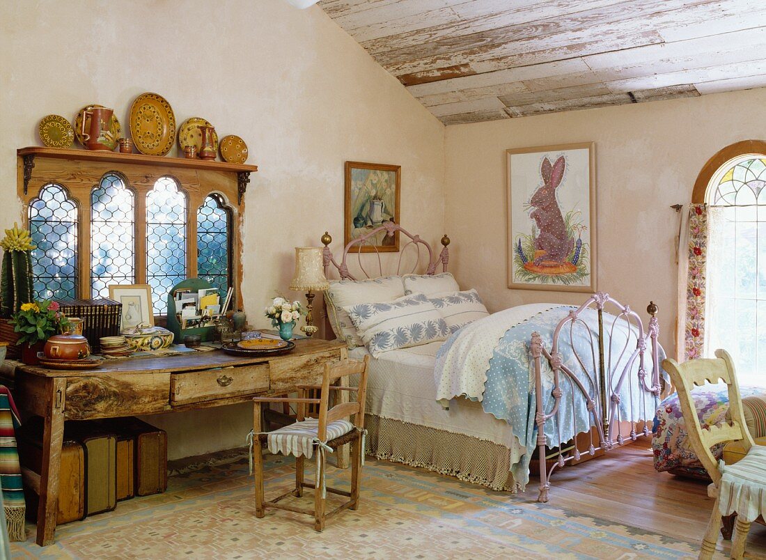 Charmantes Jugendstilbett neben antikem Wandtisch vor traditionellem Landhausfenster im Dachgeschossschlafzimmer
