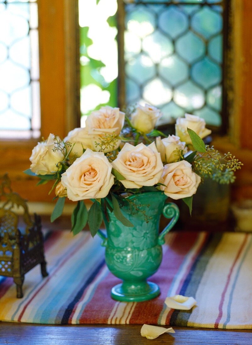 Bouquet of roses in a turquoise terra cotta vase on a striped table runner