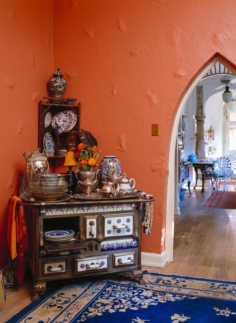 Zum Geschirrschrank umfunktionierter Holzherd vor orangefarbener Wand mit Spitzbogendurchgang