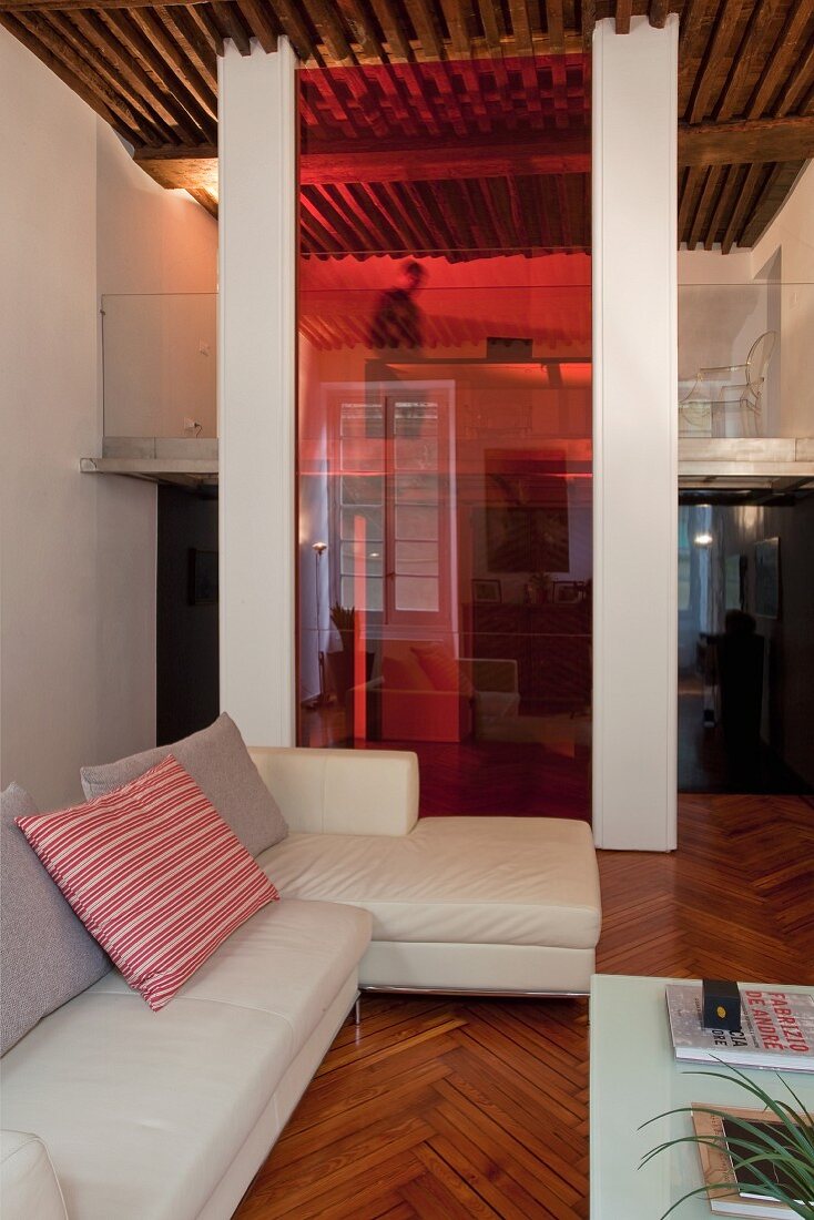 Moderne Loungeecke mit weisser Sofagarnitur vor eingefärbter Glastrennscheibe und Blick auf Galerie in offenem Wohnraum mit traditionellem Flair