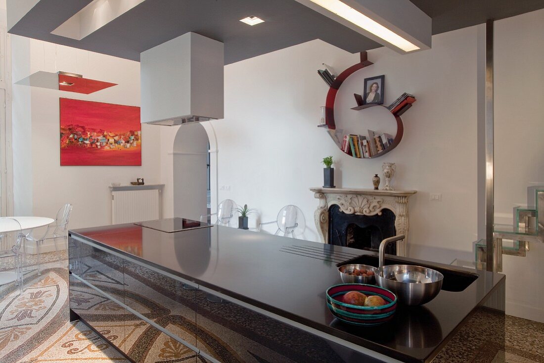 Monolithartiger Küchenblock in Schwarz vor offenem Kamin in offenem Wohnraum mit Terrazzoboden