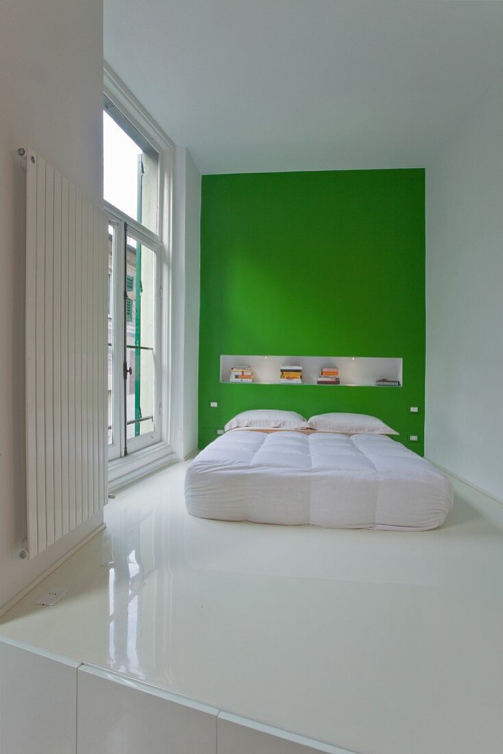 Modernes Bett mit weißem Bettüberzug vor grüner Wand und weisser Kunstharzboden