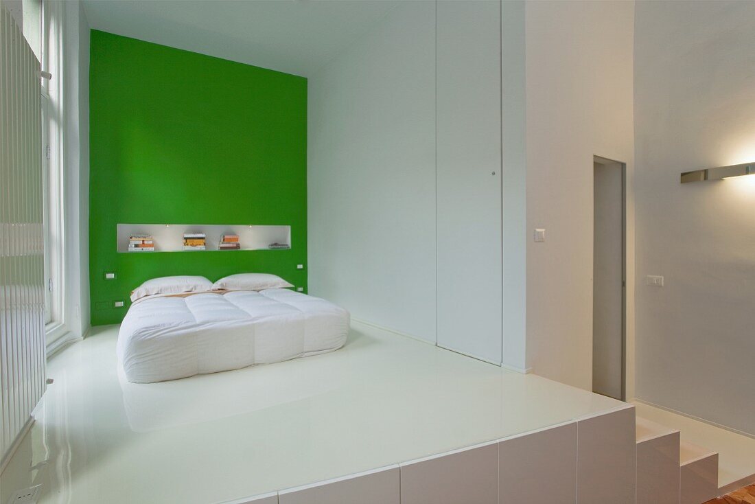 Schlafbereich auf Empore mit weißem Kunstharzboden und Bett vor grüner Wand