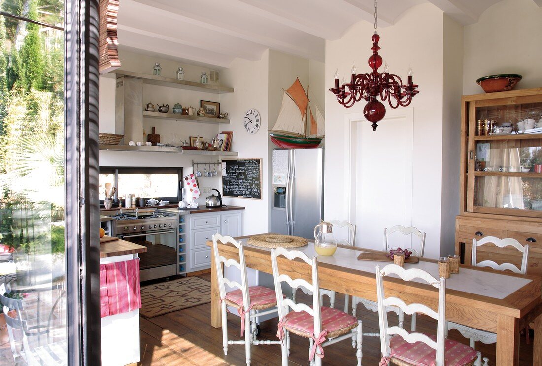 Naturholzmöbel in einfacher Wohnküche mit mediterranem Flair durch gedrechselte Holzstühle und einen Kronleuchter aus rotem Glas