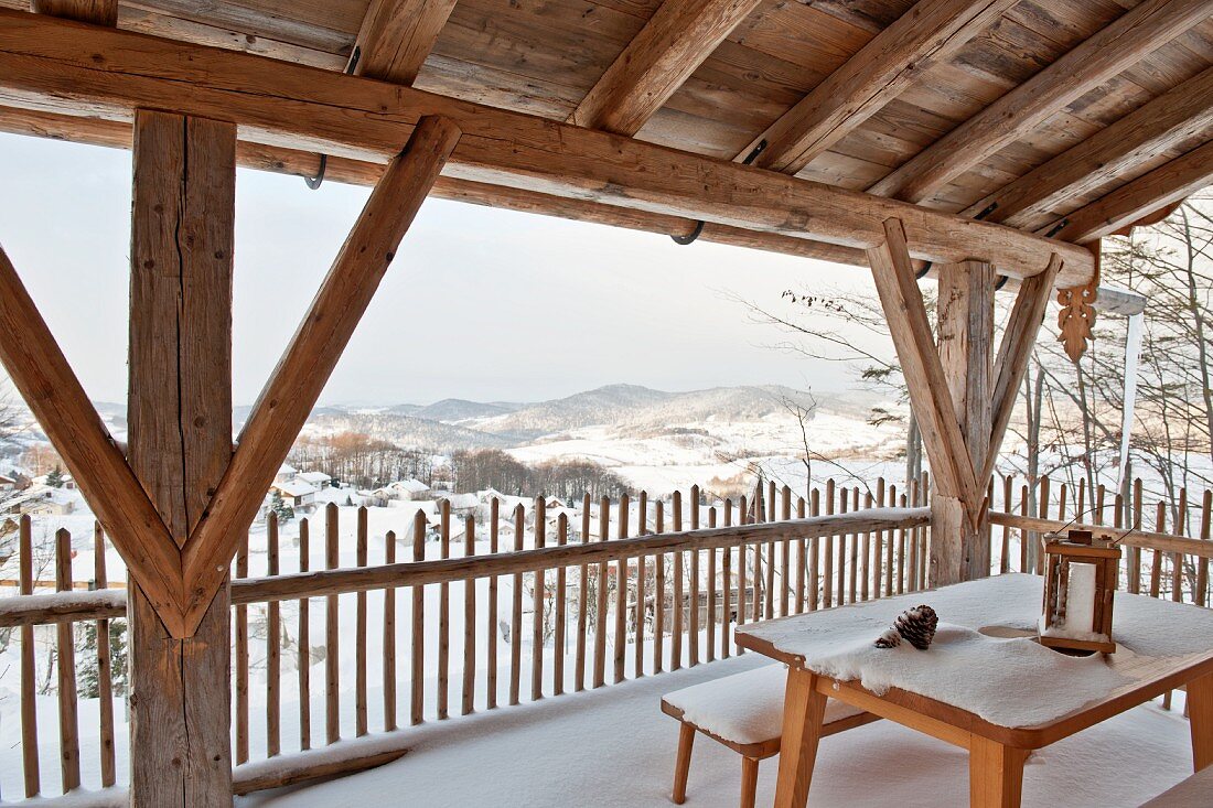 Wooden furniture and snow on roofed terrace in mountain landscape