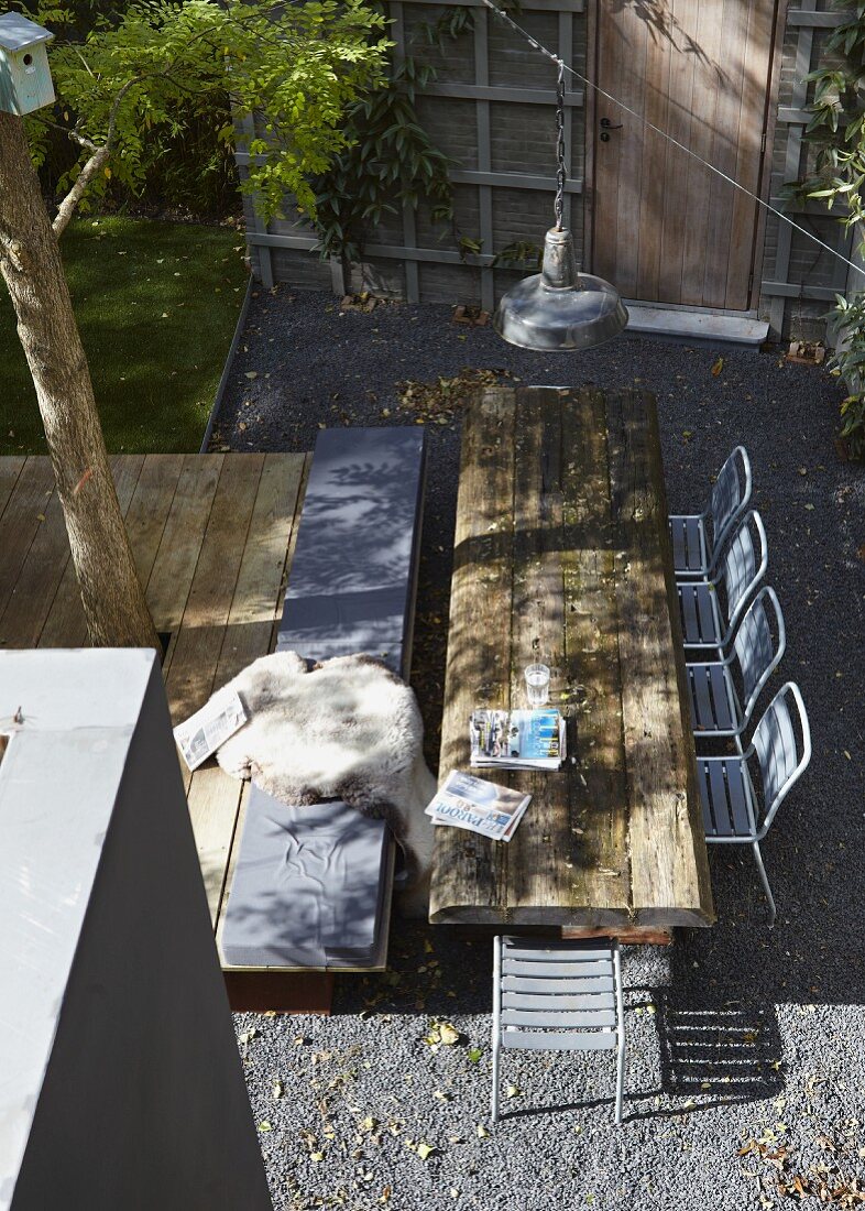 Blick von oben auf Tisch aus rustikalen Holzbohlen und Metall Terrassenstühle auf Kiesboden in sonnenbeschienen Stadtgarten