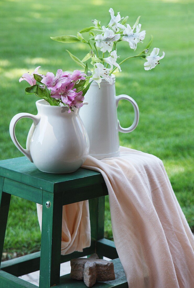 Two jugs of flowers on wooden stool in garden