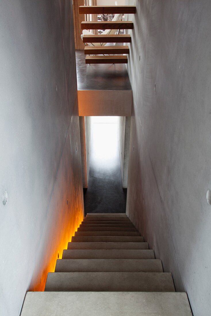 Treppenachse in Betonhaus - monolithische Betontreppe mit indirekter, farbiger Beleuchtung und auskragende Holzstufen