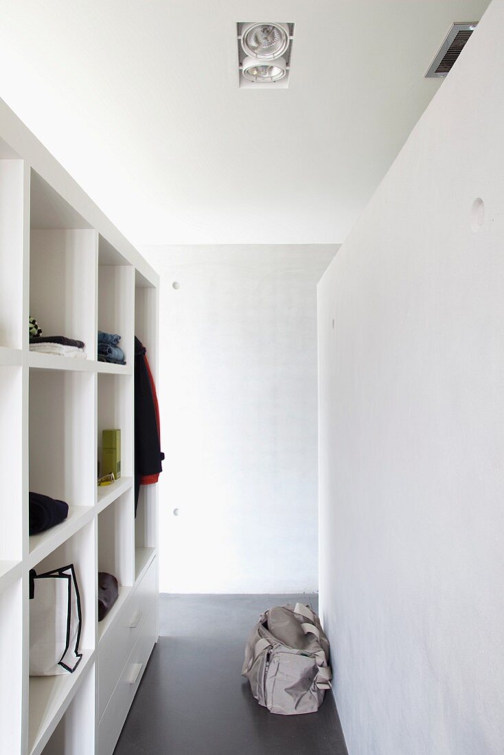 Narrow corridor with open-fronted shelves used as walk-in wardrobe; sports bag on polished concrete floor