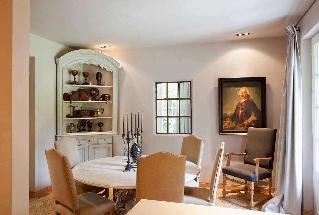 Elegant, country-house-style dining area with antique armchair below historical portrait on wall