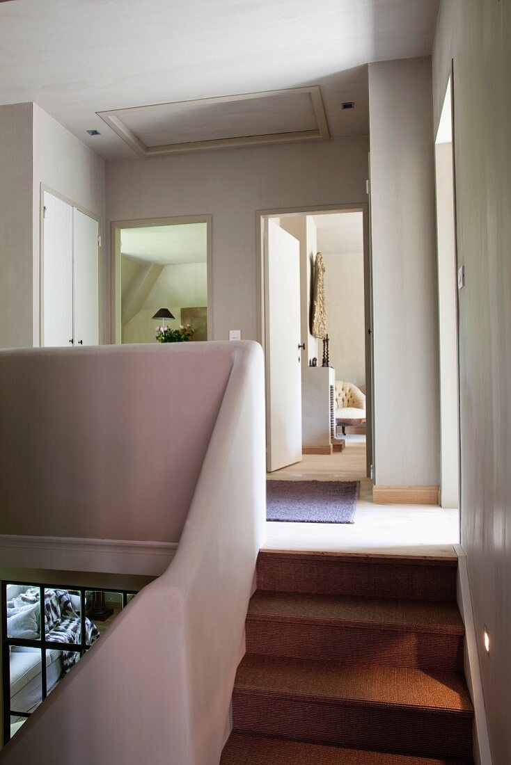 Treppenaufgang und Galerie mit organisch geformter Brüstungsmauer; offene Zimmertüren im Hintergrund