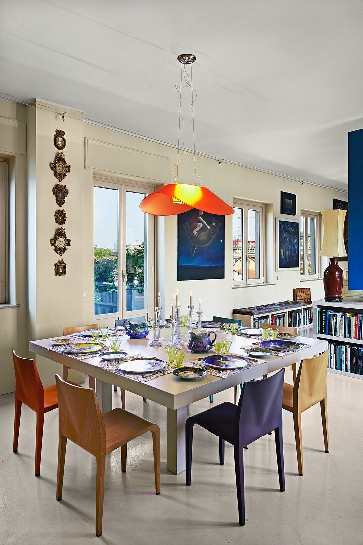 Place settings on modern dining table below pendant lamp with red lampshade in open-plan interior