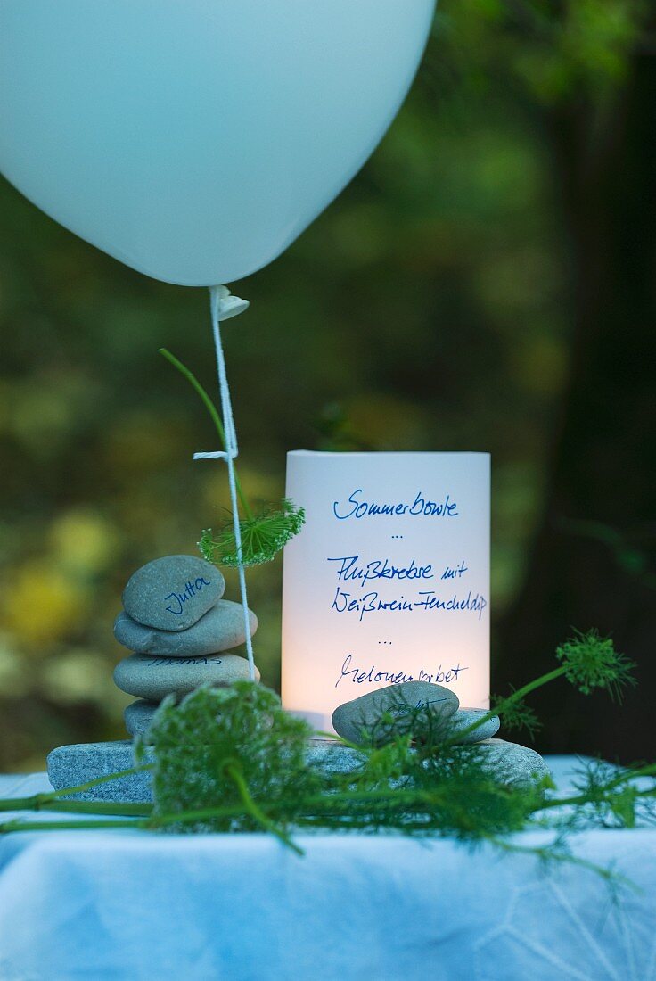 Menükarte für eine Sommerparty am Flussufer, als Tischdeko gestapelte Kieselsteine mit Namen, Luftballon und Fenchelgrün