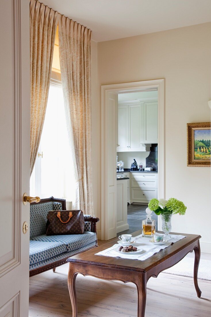 Rokoko Couchtisch und antike Sitzbank in Zimmerecke vor Fenster und Blick durch offene Tür in die Küche