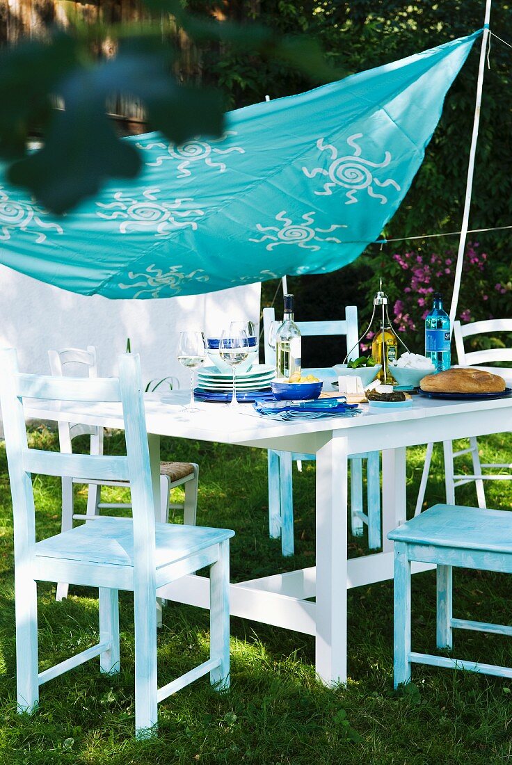 Mit Schablonenmuster bemaltes Tuch als Sonnensegel über gedecktem Tisch im Garten
