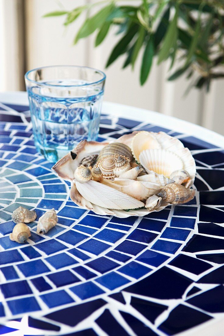 DIY balcony table with mosaic tiles in shades of blue and decorative collection of seashells