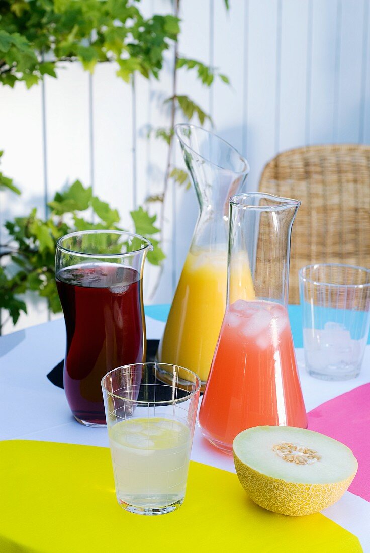 Fruit juice drinks cooled with ice cubes in glass decanters on summery garden table set with bright colours