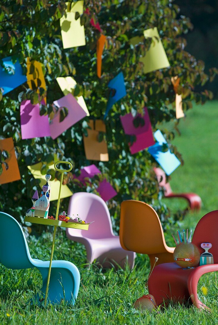 Brightly coloured plastic chairs below tree with paper decorations