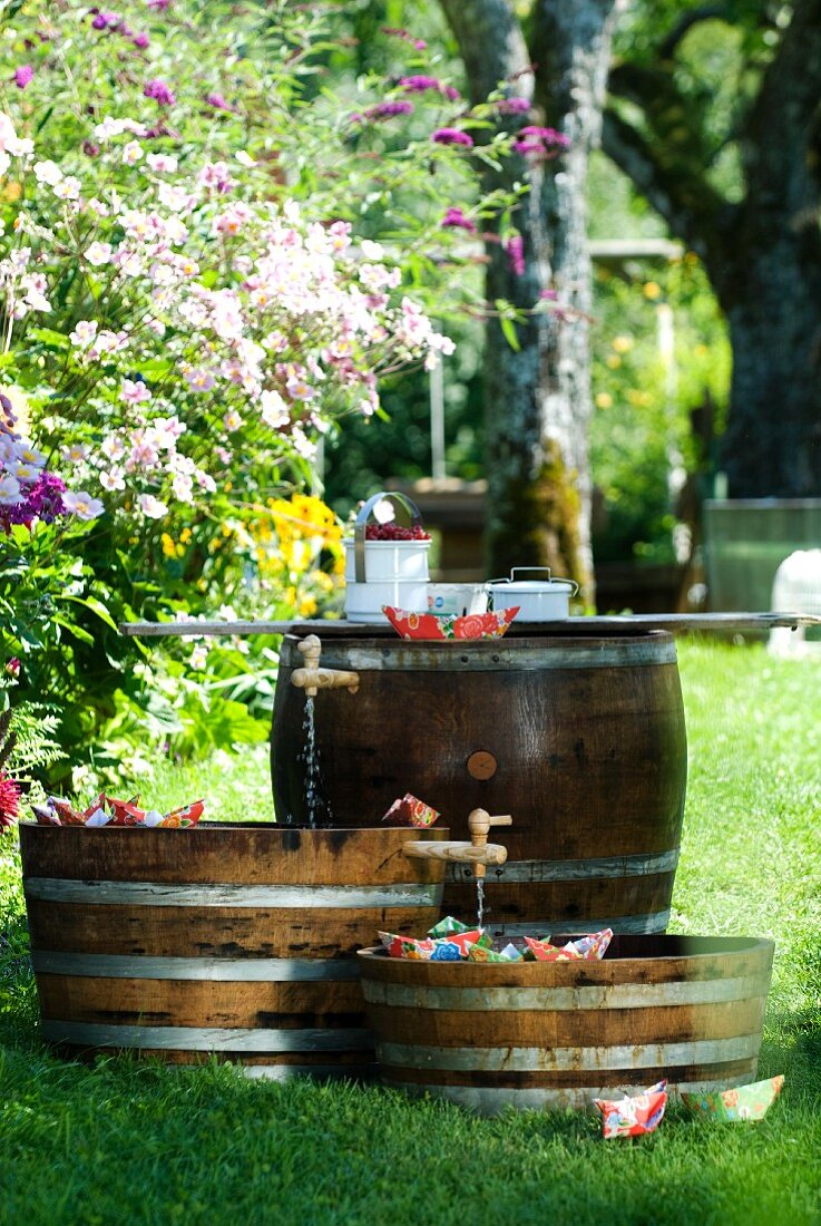 Mini-Teiche in Holzfässern mit Papierschiffchen für ein Gartenfest