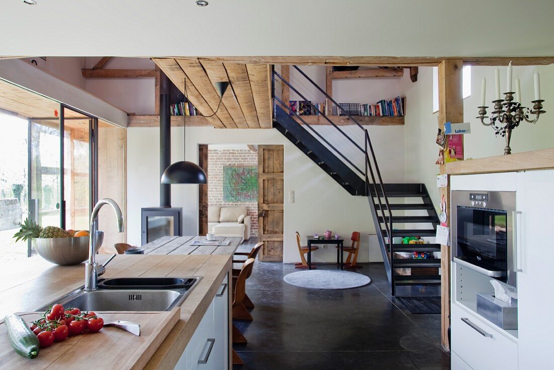 Renoviertes Haus mit offenem Wohn-Essraum und integrierter Küche, im Hintergrund führt eine Metalltreppe zum Obergeschoss