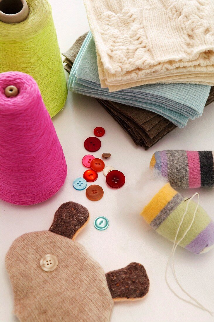 Colourful spools of thread, buttons and knitted fabrics on white surface