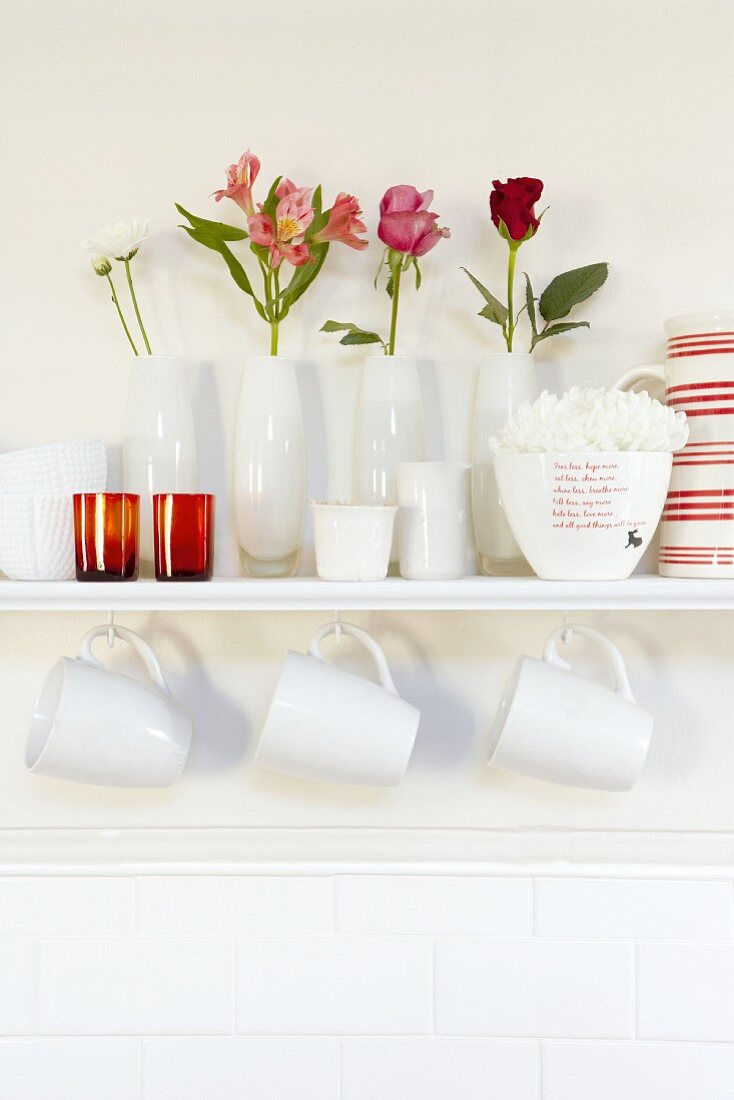 Weisses Wandregal mit Blumenvasen und Tassen am Haken
