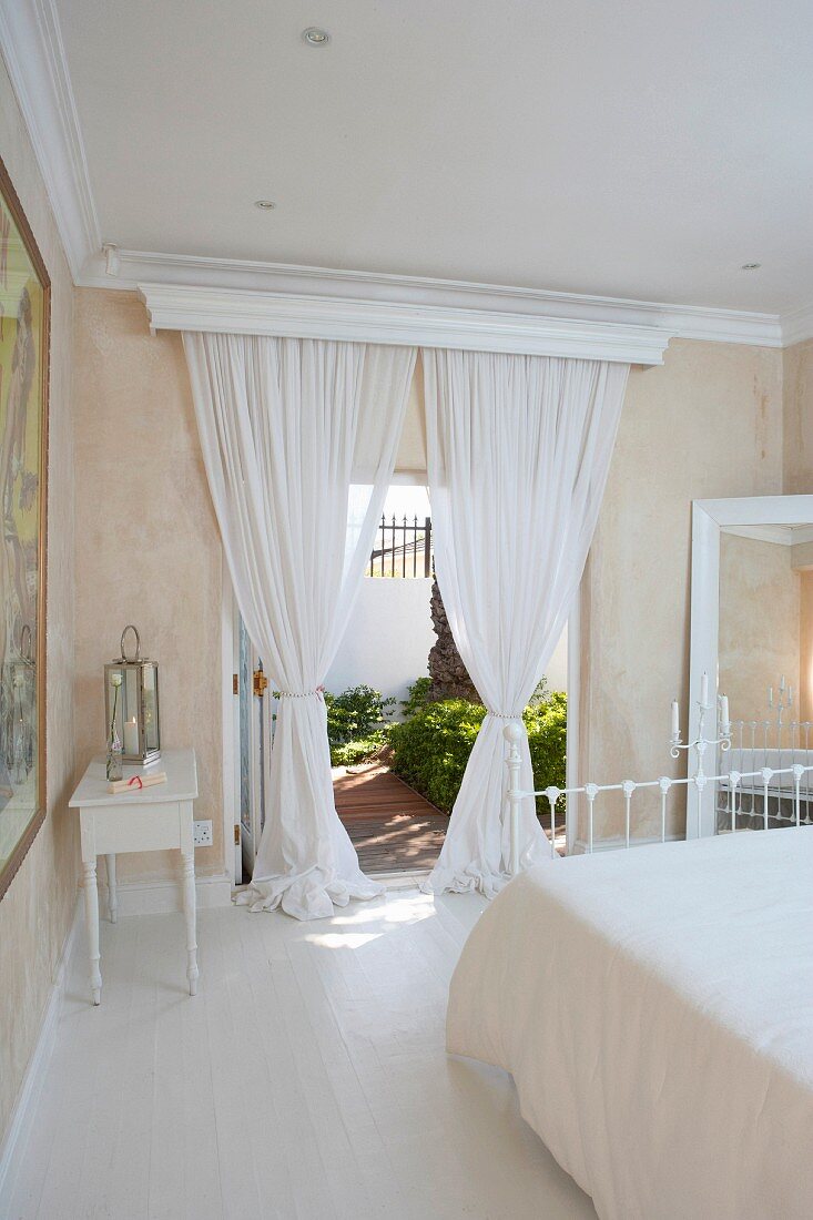 Romantisches Schlafzimmer in mediterraner Villa - weiße, luftige Vorhänge an geöffneten Terrassentüren