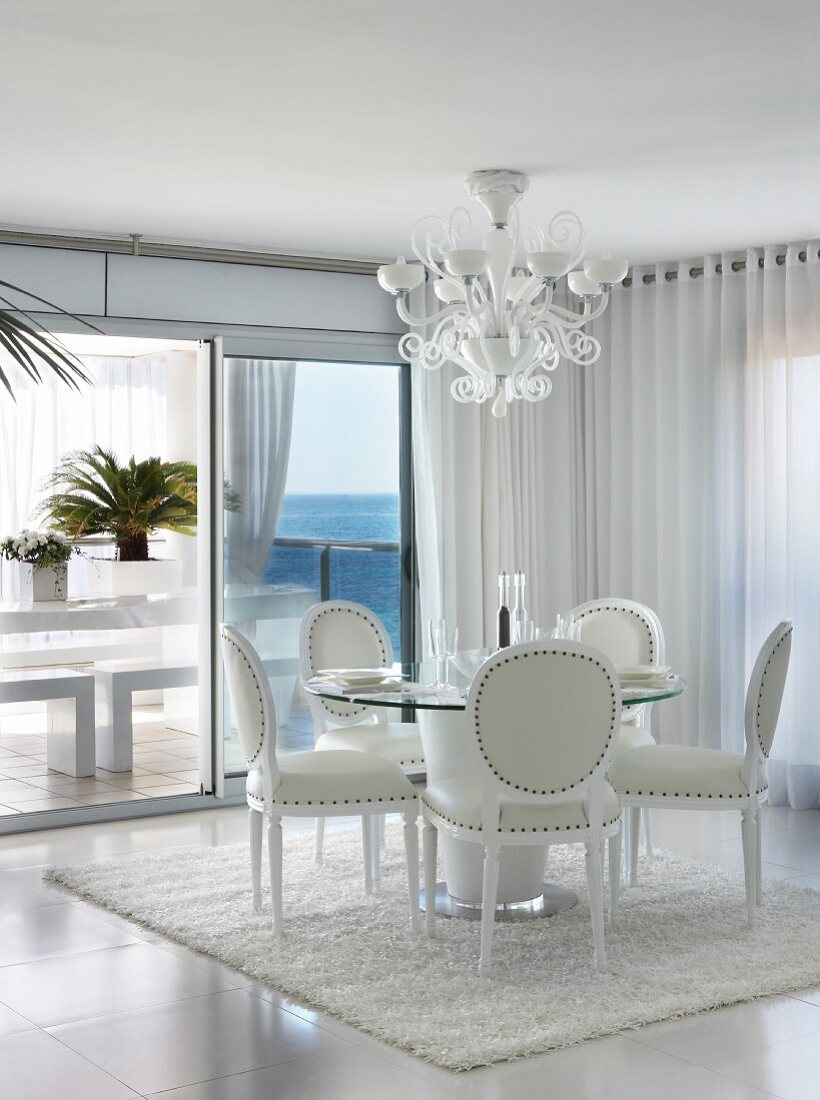 Elegant white leather chairs at round dining table in modern dining room with glass wall and sea view