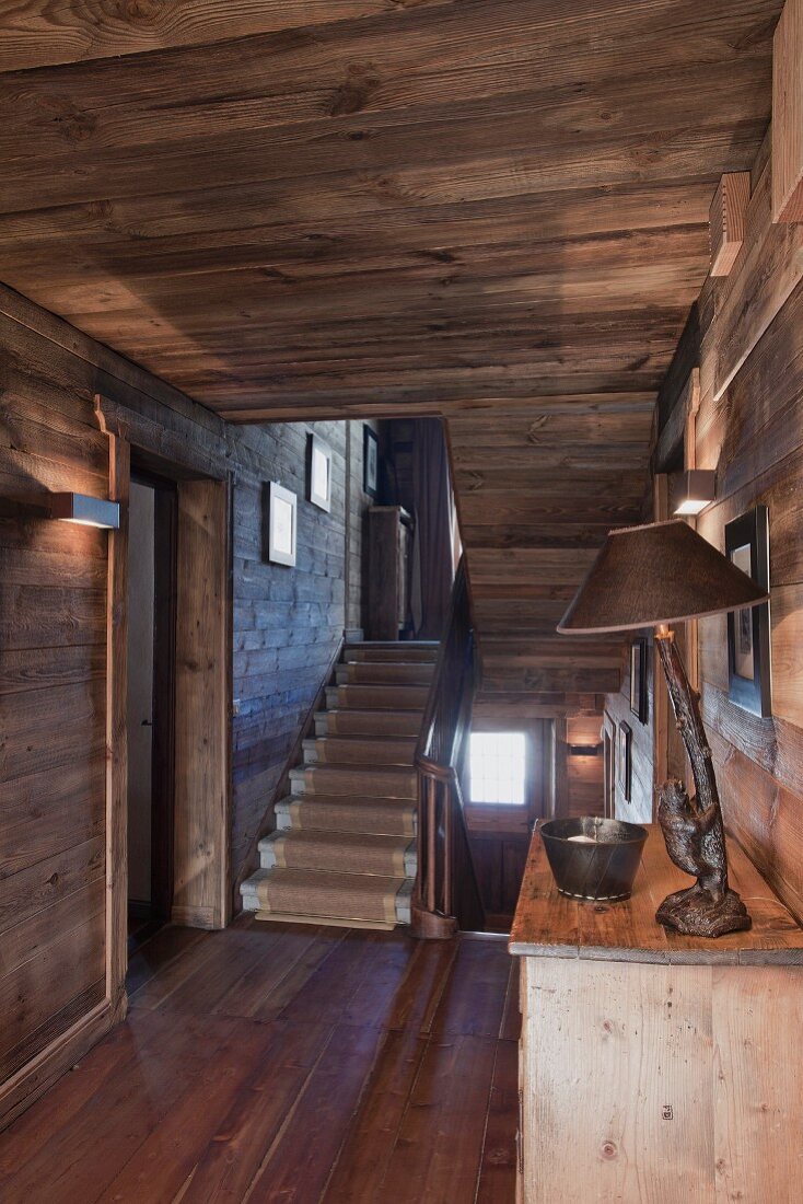 Blick vom holzverkleideten Flur mit Holzdecke und -boden in helles Treppenhaus mit Steintreppe