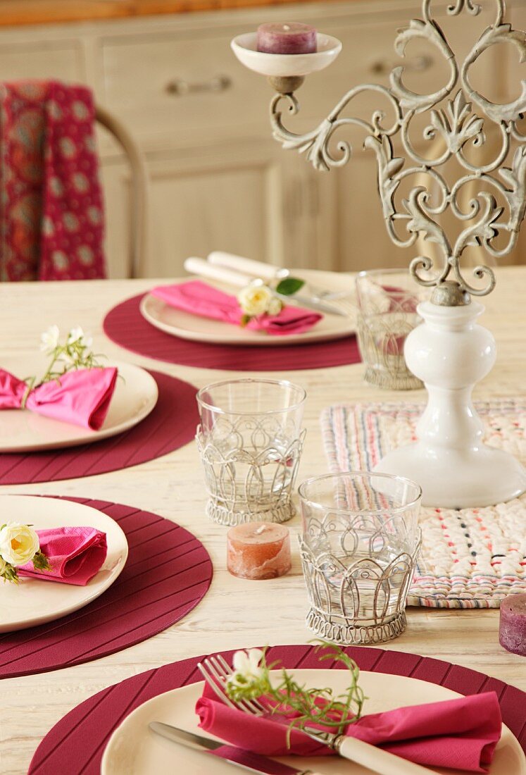 In Pink/Bordeau festlich gedeckter Tisch mit modernen Sets, kunsthandwerklich gearbeiteten Glashaltern aus Metall und romantischem Kerzenständer