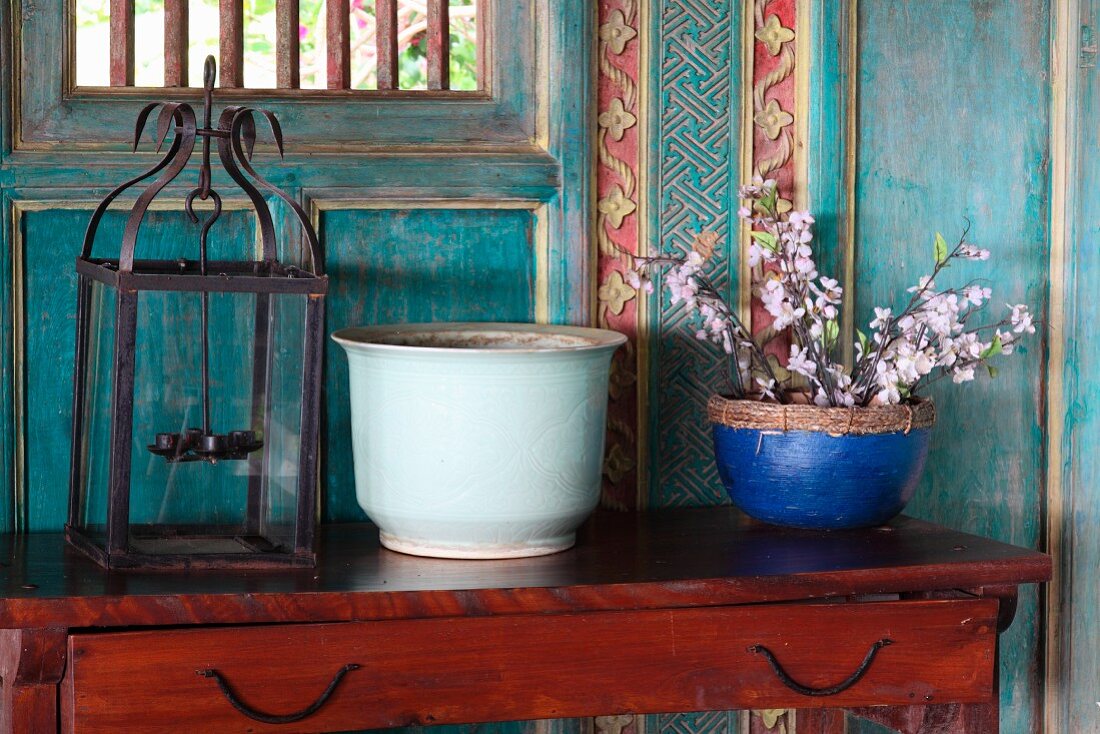 Flowering twigs in blue pot and lantern on antique console table against painted and carved wooden wall