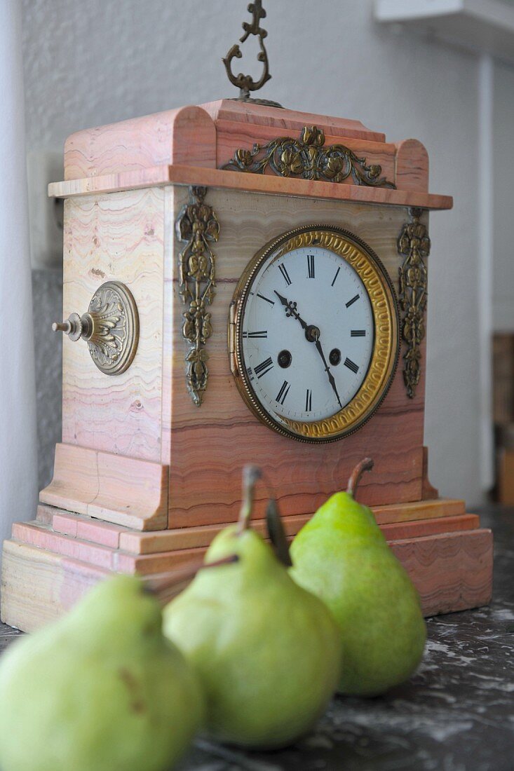 Green pears in front of antique clock on shelf