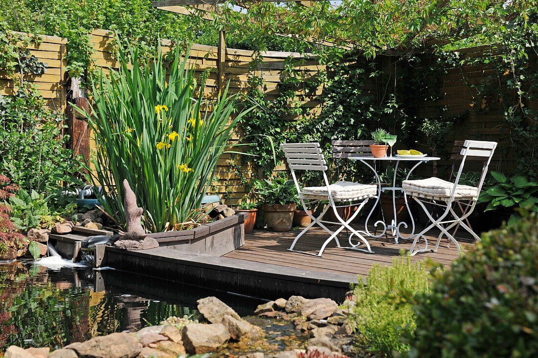 Gartenecke mit bewachsenem Holzzaun und Holzdeck mit Tisch und Stühlen neben kleinem Teich
