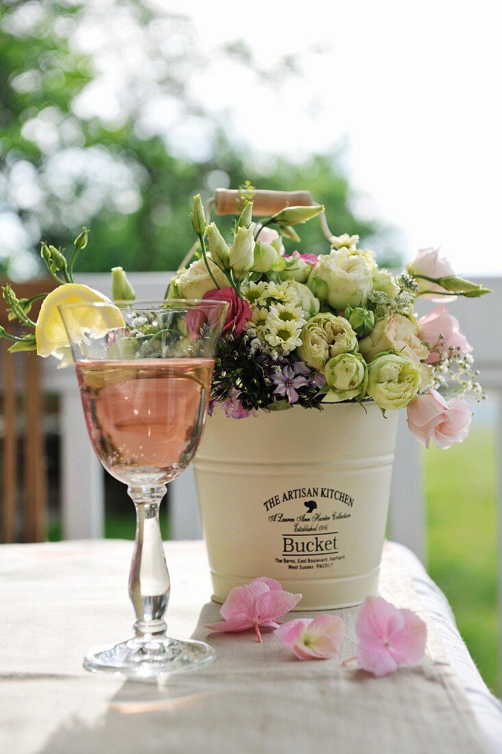 Refreshing drink and bouquet in metal bucket on table