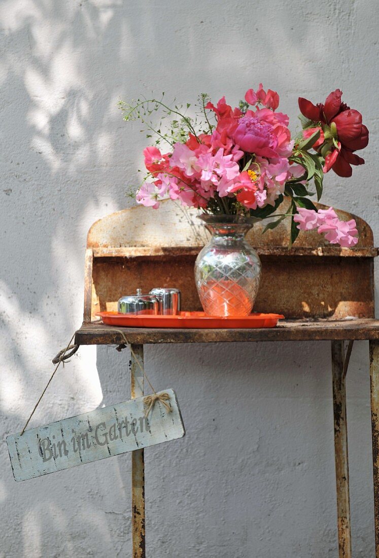 Blumenstrauss auf rostigem Vintage Gartentisch vor Hauswand