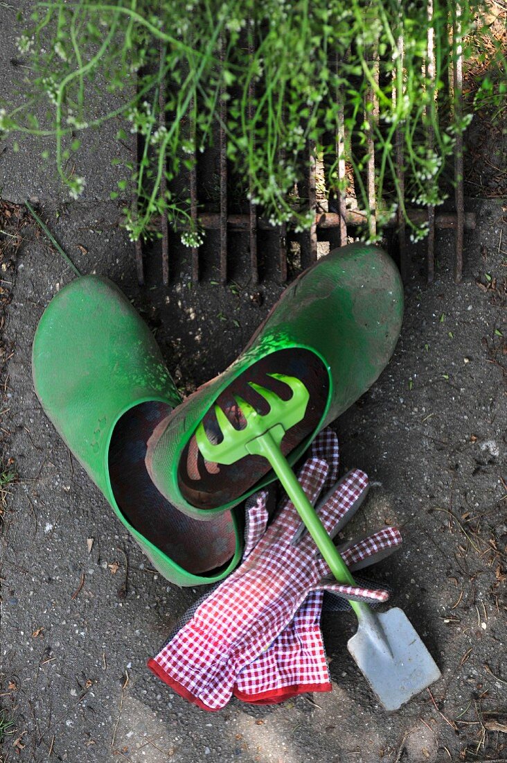 Stillleben mit Gartengerät und Handschuhen neben Gartenschuhen