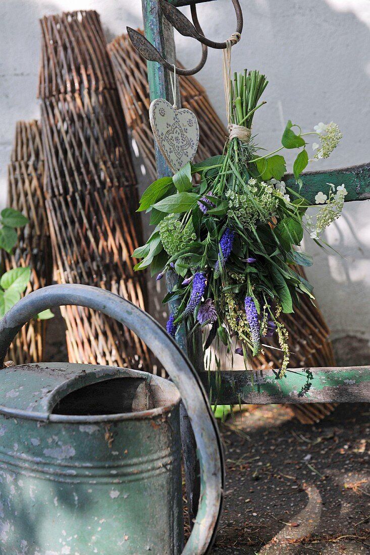 Watering can in front of a wooden ladder with a flower bouquet hanging on it