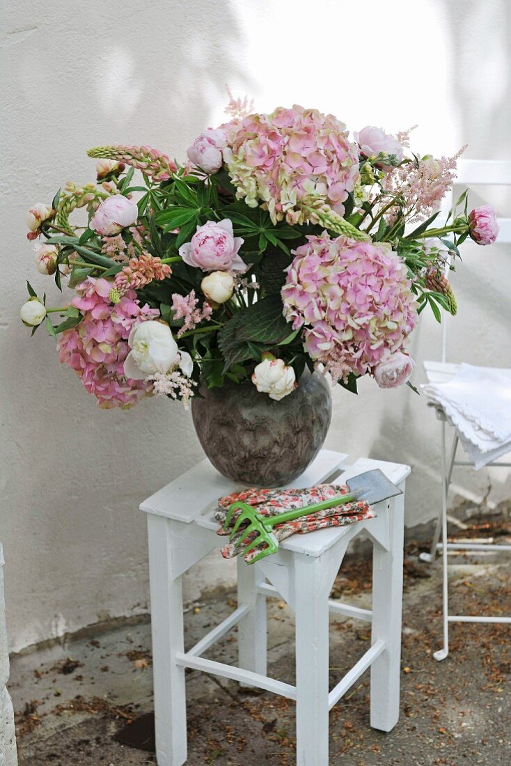 Hortensienstrauss in Vase auf weiss lackierten Hocker vor der Hauswand