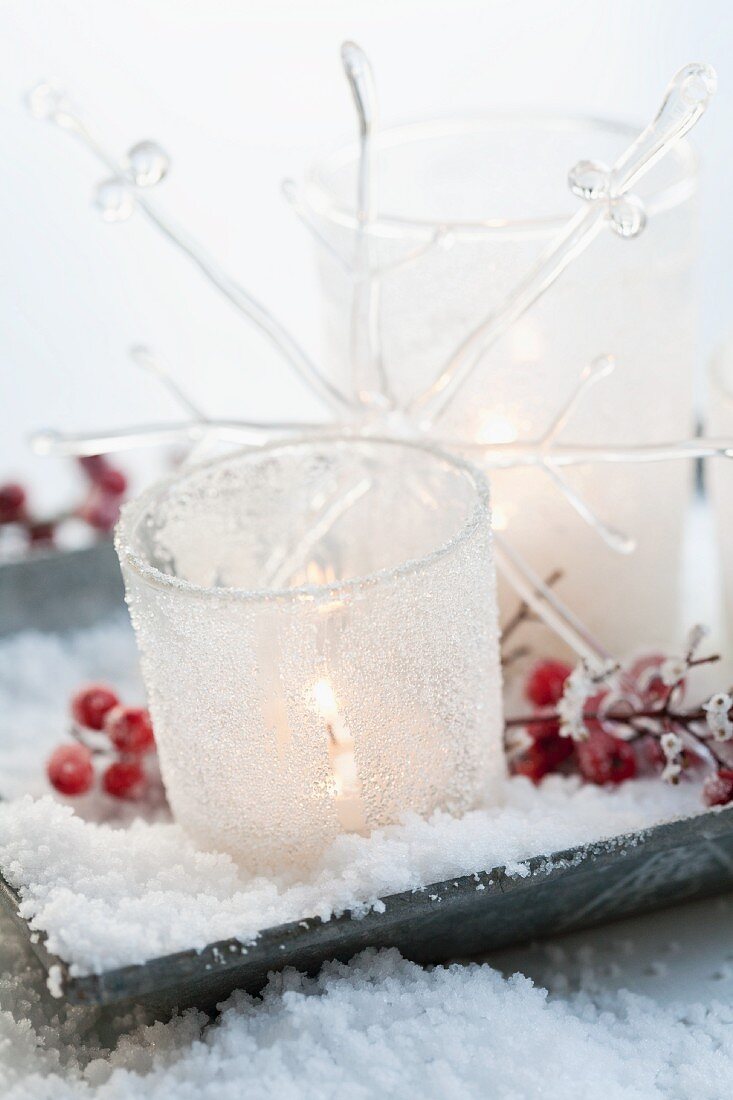 Dish holding lit tea lights in glasses decorated with artificial snow and red holly berries
