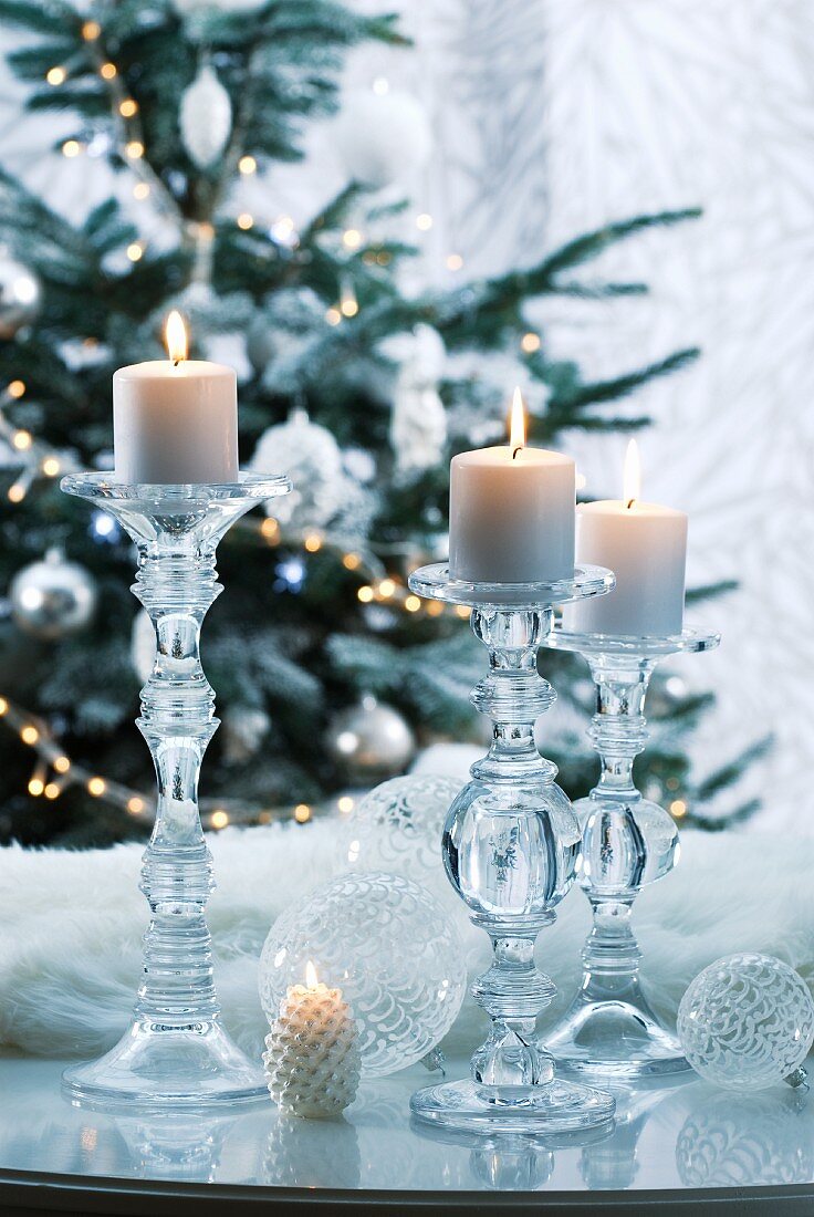 Lit candles in glass candlesticks in front of Christmas tree