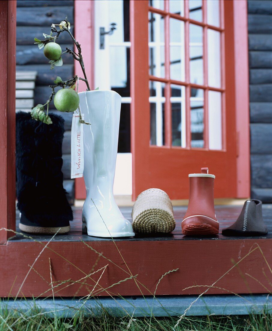 Auf die Terrasse gestellte Schuhe und Stiefel und Stiefelvase mit Apfelzweig warten auf den Nikolaus
