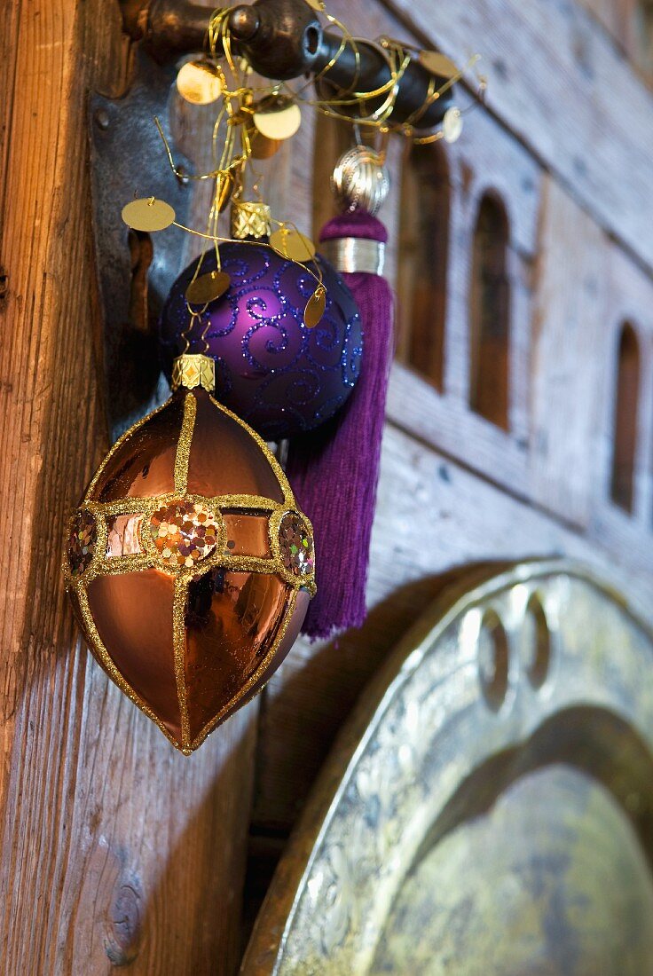 Ein kupferfarbener Anhänger, Kugel und Quaste in Violett als exotischer Weihnachtsschmuck an geschmiedeter Türklinke