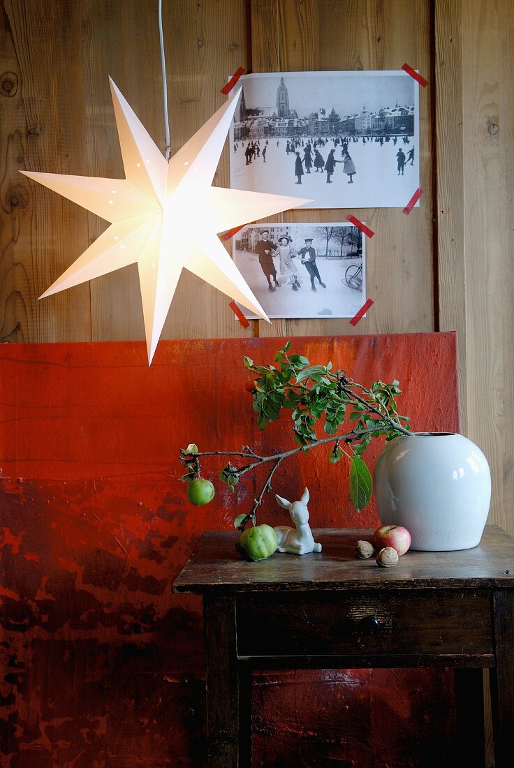 Star-shaped lantern in front of black and white postcards on wooden wall and above twigs on side table