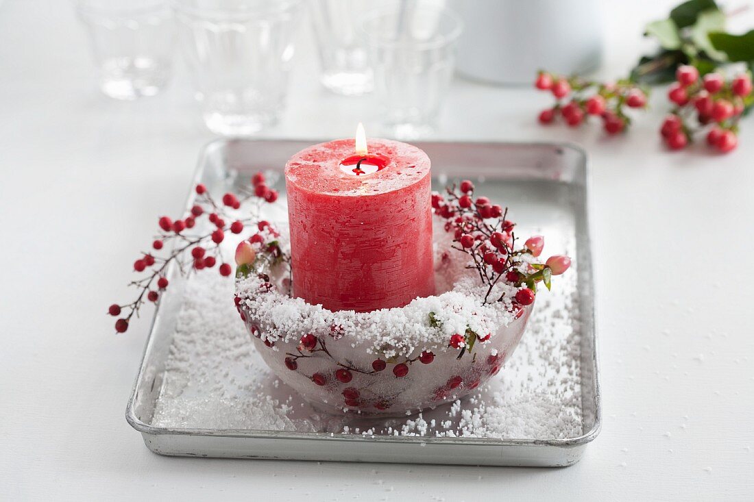Rote Kerze in einer Eisschale mit Johanniskraut- und Skimmia-Japonica-Beeren und Kunstschnee