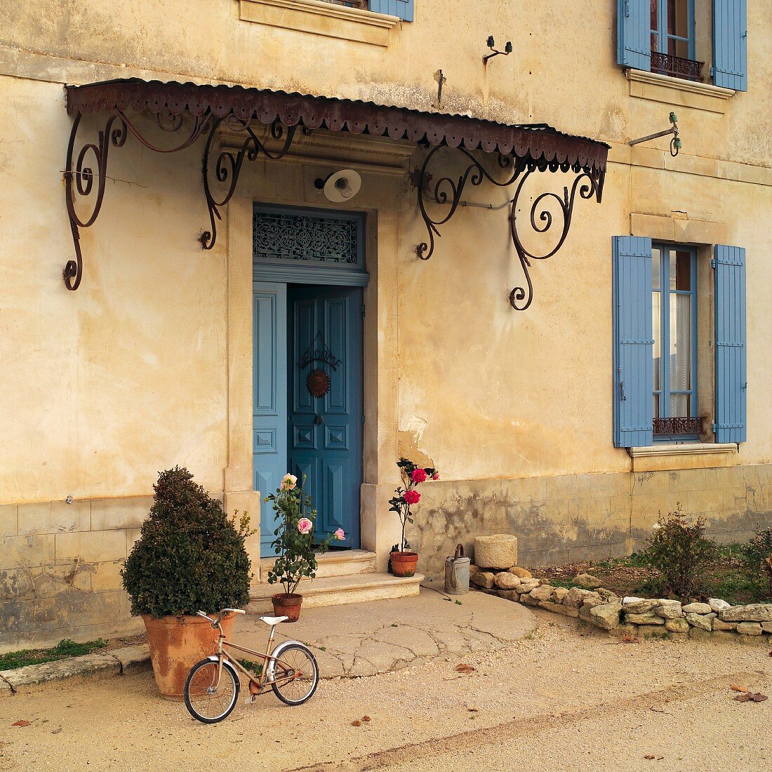 Verspieltes Metallvordach und blau gestrichene Holzelemente zur ockerfarbenen Fassade eines alten, französischen Landhauses